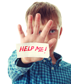 A picture of a young boy holding a piece of paper saying help me to the viewer