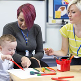A picture of two adults teaching a child in a classroom setting